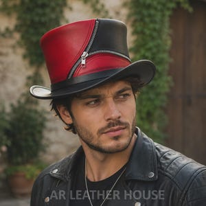 May include: A top hat featuring a split design of red and black leather. The hat is accented with a silver-toned metal zip that runs diagonally across the crown, separating the two colours. It has a wide, curved brim and a structured cylindrical shape.