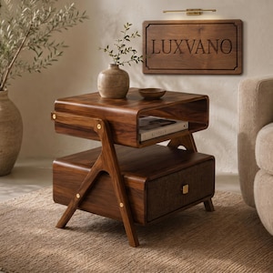 May include: A dark wood nightstand featuring a top open shelf containing a book, a lower drawer with a square gold handle, and angled legs with gold hardware accents. The nightstand is constructed from wood with a visible grain and a smooth finish.