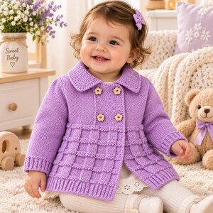 Può includere: Un cardigan in maglia color viola chiaro caratterizzato da un'abbottonatura doppiopetto con quattro bottoni in legno a forma di fiore, un colletto classico e un motivo a griglia testurizzato sulla parte inferiore, con polsini e orlo a coste.