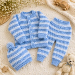 Può includere: Un set in maglia di tre pezzi composto da un cardigan a maniche lunghe con chiusura a bottoni, pantaloni abbinati con polsini a coste e un berretto con un pompon sulla parte superiore. L'intero set presenta un motivo a righe orizzontali azzurre e bianche.