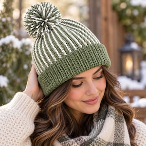 Può includere: Un berretto in maglia con una trama a coste e strisce verticali alternate in verde oliva e bianco. Il cappello presenta un ampio risvolto piegato in tinta unita verde oliva ed è sormontato da un grande pon-pon rotondo in filato misto.