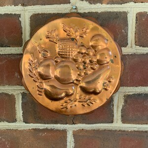 May include: A copper-colored, round, decorative mold for baking. The mold has a raised design of fruit and leaves.