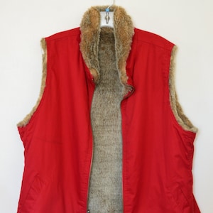 May include: A red sleeveless vest with a brown faux fur lining. The vest has a zipper closure and a stand-up collar.
