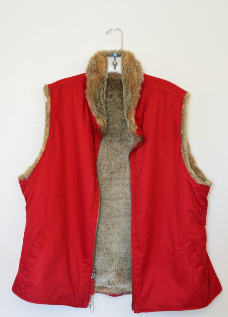 May include: A red sleeveless vest with a brown faux fur lining. The vest has a zipper closure and a stand-up collar.