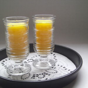 May include: Two clear glass candle holders with yellow candles on a black tray with a white doily.