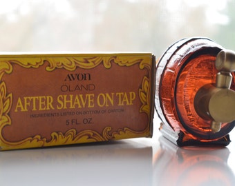 May include: Vintage Avon Oland After Shave On Tap bottle and box. The amber-colored glass bottle is shaped like a barrel with a brass-colored tap. The box is brown and yellow with the text "AFTER SHAVE ON TAP" and "5 FL. OZ."