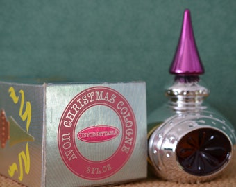 May include: A vintage Avon Christmas Cologne bottle and box. The silver-colored bottle has a magenta-colored conical top. The box is silver with a red and pink label that reads "Christmas Cologne" and "Unforgettable".
