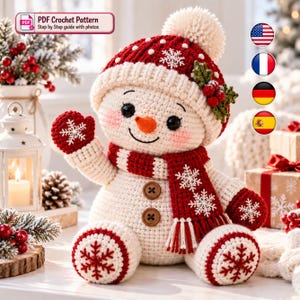 Puede incluir: Un muñeco de nieve de ganchillo con cuerpo blanco, gorro rojo con pompón blanco y patrón de copos de nieve, bufanda roja con detalles de copos blancos y dos botones marrones en el pecho. Tiene una nariz naranja y manoplas rojas.