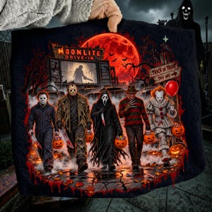 May include: A black fabric item featuring a graphic print of five horror movie characters walking together. The scene includes a red moon, a Moonlite Drive-In sign, and a Trick or Treat sign. Each character carries a pumpkin-shaped candy bucket.