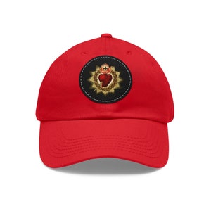 May include: Red baseball cap with a black and gold embroidered patch featuring a heart with a crown of thorns and a cross.