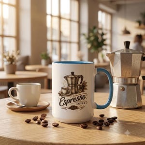 May include: A white ceramic mug with a light blue interior and handle, featuring a brown graphic illustration of a moka pot, a small cup of coffee, and coffee beans with the text Espresso LOVER printed in a decorative script font.