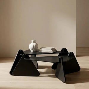 May include: Two black triangular coffee tables with flat surfaces and vertical support panels. A white ceramic vase and a stack of two books sit on the higher table. The text "DESIGNED TO DEFINE SPACE" is printed at the bottom of the image.
