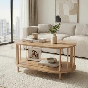 May include: An oval light wood coffee table with a slatted base design and a lower shelf. The table surface holds a book titled Art Book, a small geometric object, and a white vase with a green plant. A photo frame and a book sit on the lower shelf.