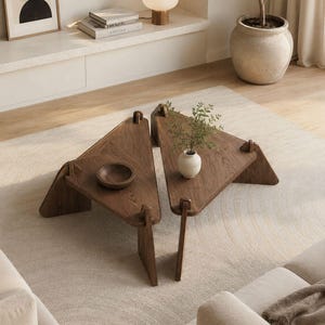 May include: Two triangular coffee tables crafted from dark brown wood with visible grain patterns. Each table features three angled legs that slot into the tabletop corners. A small wooden bowl sits on one table and a white vase on the other.