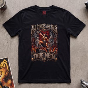 May include: A black short-sleeve t-shirt featuring a graphic print of a muscular warrior holding a weapon, surrounded by flames and banners. The text "ALL OTHERS ARE FALSE" and "TRUE METAL" is printed in a metallic font above and below the figure.