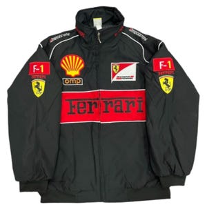 Könnte beinhalten: Eine schwarze Reißverschlussjacke mit einem markanten roten horizontalen Streifen auf der Brust, der den Schriftzug Ferrari in schwarzer Schrift trägt. Die Jacke ist mit verschiedenen gestickten Aufnähern wie Shell, Scuderia Ferrari, F-1 und Bridgestone versehen.
