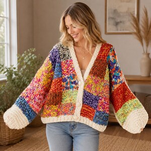May include: A chunky knit cardigan featuring a patchwork design of multicoloured yarn squares in shades of red, blue, yellow, and purple. The garment has long sleeves, a V-neckline, and a thick cream-coloured border with three matching buttons.