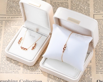 Op de afbeelding: Een gouden ketting met bijpassende oorbellen en een gouden armband, elk voorzien van marquise-geslepen rode stenen en kleine witte accenten. De sieraden worden gepresenteerd in twee open witte doosjes, met de armband om een wit kussentje.