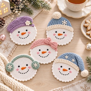 Könnte beinhalten: Fünf runde gehäkelte Schneemann-Untersetzer mit weißen Gesichtern, schwarzen Augen, orangefarbenen Nasen und rosa Wangen. Jeder Schneemann trägt ein anderes Accessoire: ein lila Barett, eine blaue Mütze mit Bommel, ein rosa Stirnband, grüne Ohrenschützer oder eine blaue Mütze.