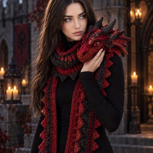 Può includere: Una lunga sciarpa all'uncinetto con una testa di drago a un'estremità, realizzata in filato rosso scuro e grigio antracite. La sciarpa presenta un motivo testurizzato simile a squame lungo tutta la lunghezza e una testa di drago dettagliata.