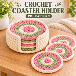 May include: A crochet coaster holder and three matching circular coasters featuring concentric rings of pink, sage green, and cream yarn. The text CROCHET COASTER HOLDER PDF PATTERN is displayed above the items on a light background.