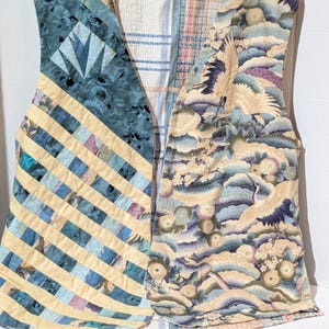 May include: A sleeveless vest featuring a patchwork design on the left side with diagonal blue and cream stripes and a floral pattern, while the right side displays a printed fabric with cranes, clouds, and flowers in blue, cream, and purple tones.