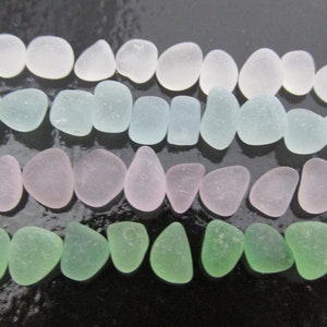 May include: An assortment of sea glass pieces in various colors, including white, light blue, pink, and green. The smooth, rounded shapes of the glass are arranged in neat rows, creating a visually appealing display. The sea glass is likely used for crafts or jewelry.