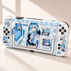 May include: A white handheld gaming console featuring a light blue theme with various anime-style character illustrations, pixelated heart graphics, and Japanese text including "大好き", "ラジモド", "おまいゆめ", and "にこにこ". The device includes standard black buttons, joysticks, and a kickstand.