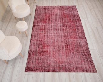 Puede incluir: Una alfombra rectangular que presenta una paleta de colores magenta intenso y rojo oscuro con una textura desgastada y descolorida. La alfombra muestra un patrón complejo y repetitivo en su superficie, caracterizado por zonas de desgaste.