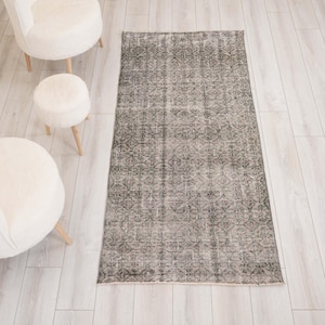 May include: A rectangular area rug featuring a repeating geometric pattern in shades of charcoal grey and off-white. The rug has a distressed, weathered appearance with a low pile texture and finished edges, laid flat on a light-coloured floor.