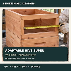 Può includere: Un melario per alveare in legno chiaro con giunzioni visibili, dotato di un metro a nastro giallo teso attraverso l'apertura interna per mostrare le dimensioni in cm. Il testo recita STRIKE HOLD DESIGNS ADAPTABLE HIVE SUPER.