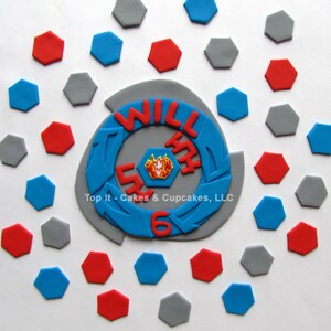 May include: A blue and gray cake topper with the words "Will Turn 6" and a red and yellow cartoon character. The topper is surrounded by gray, red, and blue hexagonal decorations.