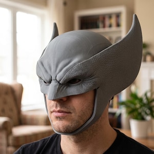 May include: A grey, textured, full-head mask featuring prominent, tall, curved ear-like protrusions extending upward from the sides. The mask has a smooth, rounded top section and a detailed, wrinkled brow area above the eye openings.