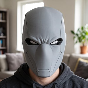 May include: A full-face gray helmet featuring a smooth, angular design with prominent brow ridges and black-rimmed eye openings. The eye sections contain a white mesh material, and the overall structure displays visible 3D printed layer lines.