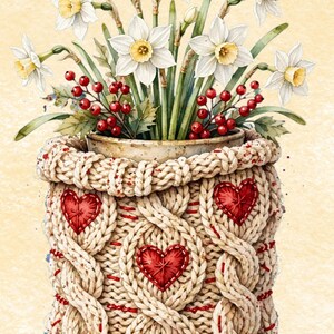 Può includere: Un coprivaso in maglia beige con trama a trecce e applicazioni a forma di cuore rosso, contenente un bouquet di narcisi bianchi con centro giallo e rametti di bacche rosse. Il design presenta cuciture rosse decorative su tutto il tessuto.