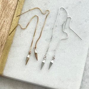 May include: Two pairs of delicate chain earrings with pointed tips. One pair is gold and the other is silver.