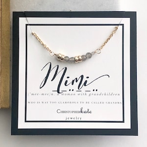 May include: A white card with black text and a gold chain with gray beads. The text reads "Mimi ('mee-mee)n, a woman with grandchildren WHO IS WAY TOO GLAMOROUS TO BE CALLED GRANDMA" and "CHRISTOPHERkate jewelry".