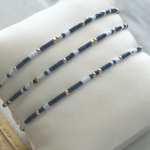 Puede incluir: Tres pulseras superpuestas con cuentas azules y blancas alternadas y detalles dorados.