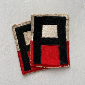 May include: Two vintage military patches with a red, white, and black design. The patches are made of felt and have a stitched border.