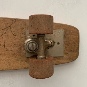 May include: A vintage wooden skateboard with two brown wheels and a silver metal truck. The skateboard has a simple design with a few lines drawn on the wood.