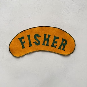 May include: A yellow felt patch with a green embroidered word "FISHER" in a curved font.