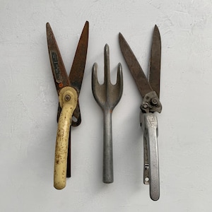 May include: A set of three gardening tools including a pair of shears with a cream-colored handle, a metal three-pronged hand cultivator, and a pair of metal hedge clippers with the text "Doo-Klip" embossed on the handle mechanism.