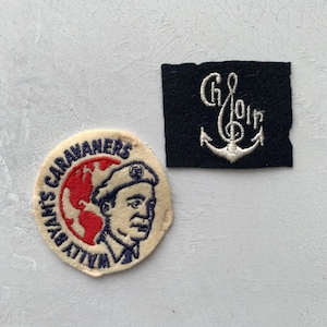 May include: Two vintage patches. One is round with a cream background, red globe, and a man's portrait with the text "Wally Byam's Caravaners". The other is a black square with white embroidered text and an anchor.