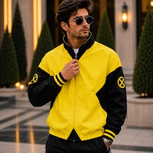 Peut inclure: Une veste zippée jaune et noire avec un col montant, des manches longues à poignets noirs et un emblème circulaire jaune et noir représentant le logo X-Men sur chaque épaule. La veste présente une fermeture éclair centrale et un design bicolore.