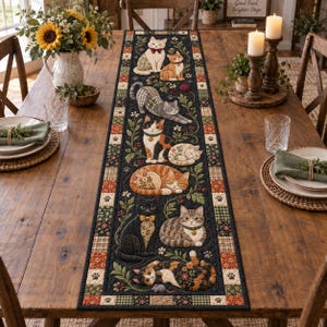 May include: A long rectangular table runner featuring a quilted design with various cats in different poses, including sitting, sleeping, and stretching. The cats are surrounded by floral vines and leaves on a dark background with a checkered border.