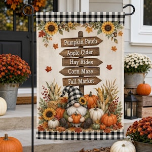 May include: A decorative garden flag featuring a black and white buffalo check border, a central wooden signpost with text reading Pumpkin Patch, Apple Cider, Hay Rides, Corn Maze, and Fall Market, surrounded by sunflowers, pumpkins, and corn.
