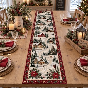 May include: A long, rectangular quilted table runner featuring a winter village scene with snow-covered houses, evergreen trees, a winding path, and a deer. The runner has a deep red border decorated with poinsettia flowers and holly leaves.