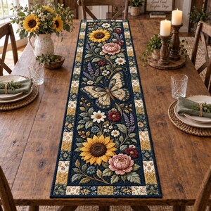 Puede incluir: Un camino de mesa rectangular con un panel central azul oscuro que presenta un estampado detallado de una mariposa grande, girasoles, peonías rosas y ramas de lavanda. El camino está bordeado por un patrón de cuadros de flores amarillas, crema y azules.