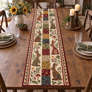 Pode incluir: Um caminho de mesa retangular de tecido com um design de patchwork com colunas alternadas de motivos florais e coelhos. O caminho tem um fundo creme com detalhes em vermelho, azul, amarelo e verde, com acabamento em borda vermelha escura.