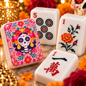 May include: Three white rectangular mahjong tiles featuring distinct designs. One tile displays a colorful sugar skull with floral accents, another shows a red number five with circular patterns, and the third features a red number one with a floral motif.